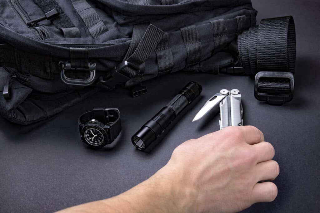 Everyday carry (EDC) items for men in black color - backpack, tactical belt, flashlight, watch and silver multi tool.